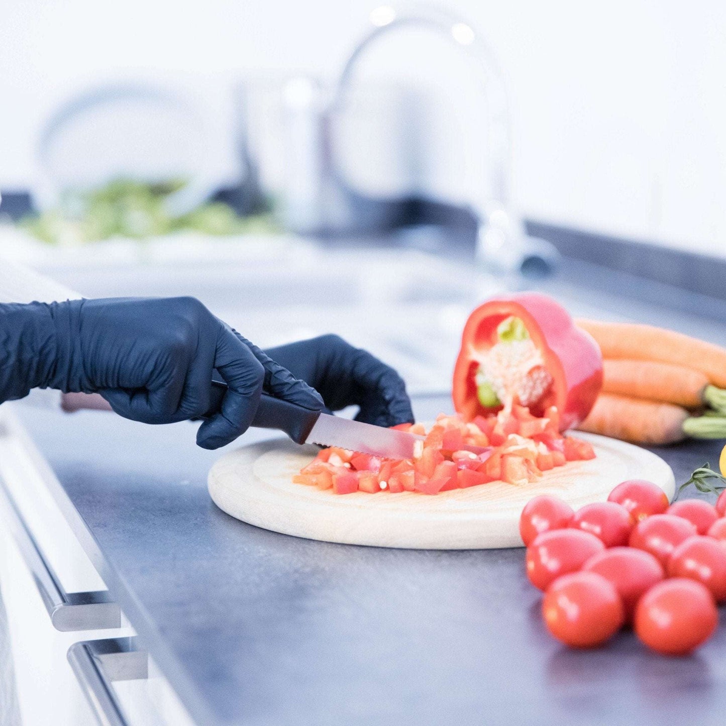 A chef knife with black handle chopping red bell pepper on white board while wearing black wave nitril handschuhe schwarz