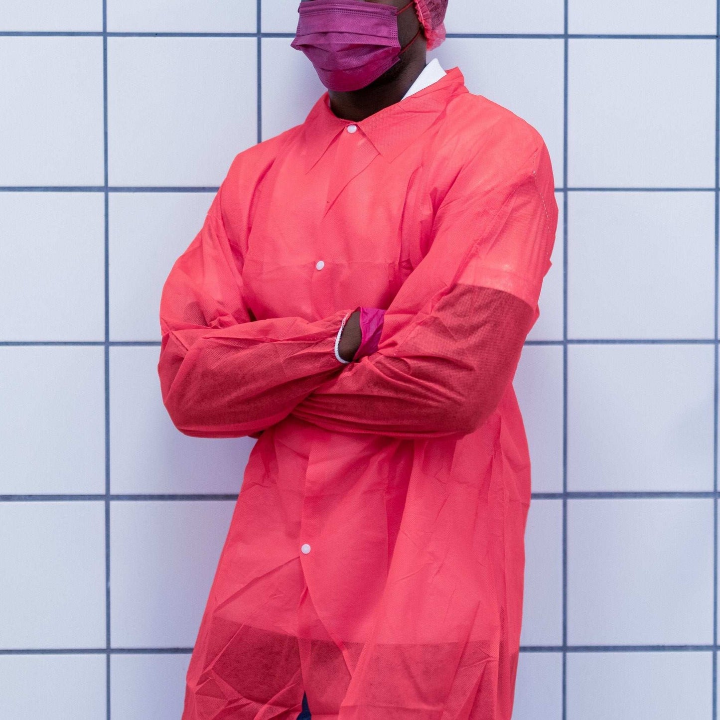 Person trägt nitras pp-besuchermantel in rot mit weißen knöpfen und passenden pinken handschuhen für hygienische und professionelle umgebungen