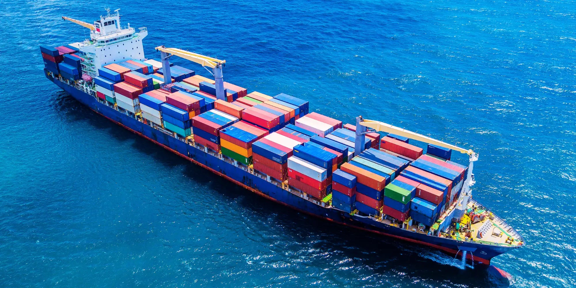 Ein blauer Containerschiff mit weißem Aufbau, das zahlreiche bunte Versandcontainer in Rot, Blau, Grün und Gelb transportiert.