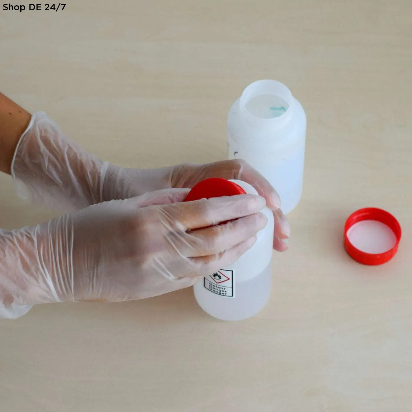 Weiße kunststoff-chemikalienflasche mit rotem deckel und gefahrensymbol für nitras vinyl und vinyl p handschuhe